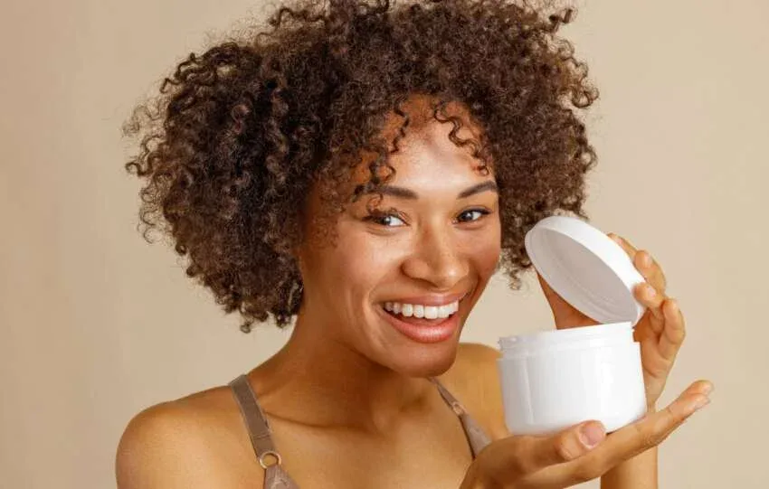 Woman with natural hair holding a homemade deep conditioner in a white jar.