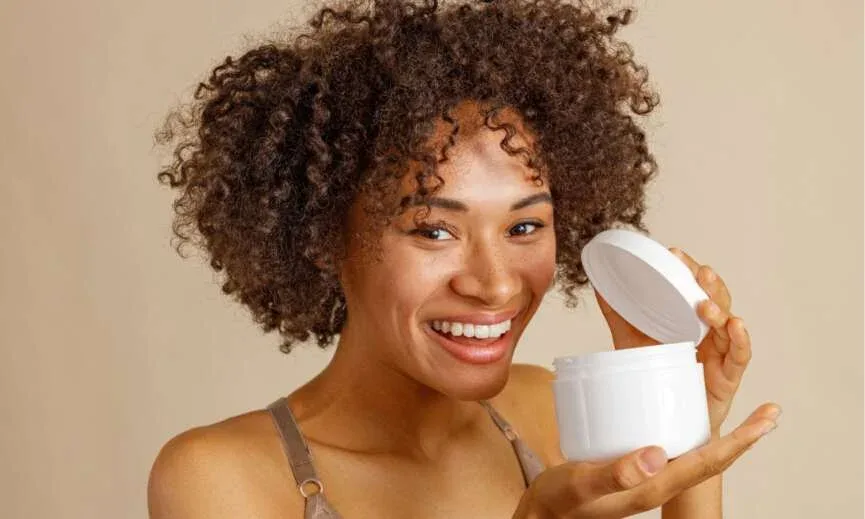 Woman with natural hair holding a homemade deep conditioner in a white jar.