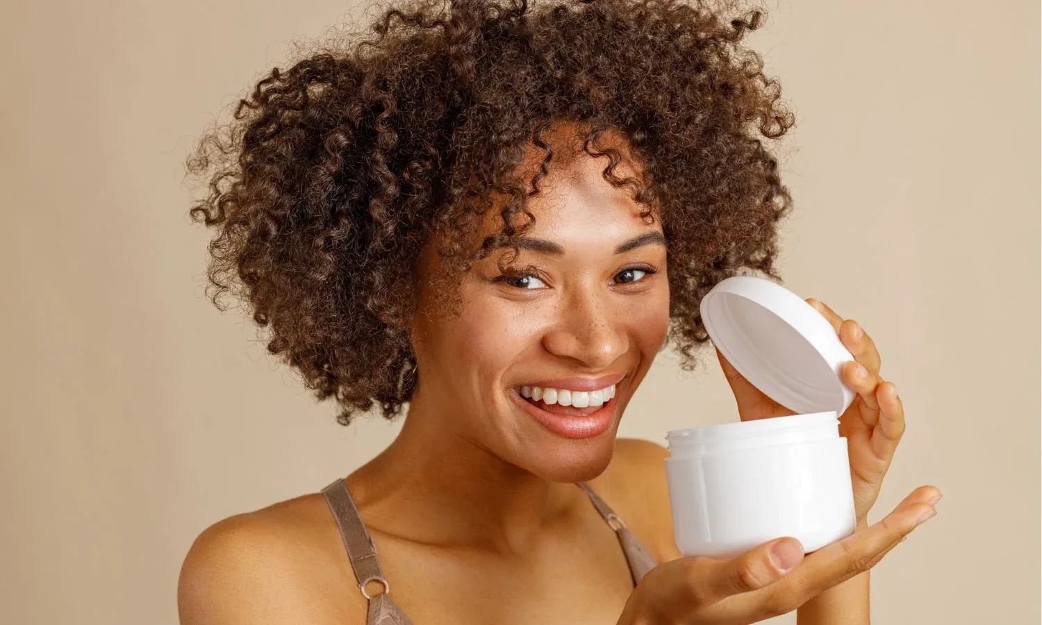 Woman with natural hair holding a homemade deep conditioner in a white jar.