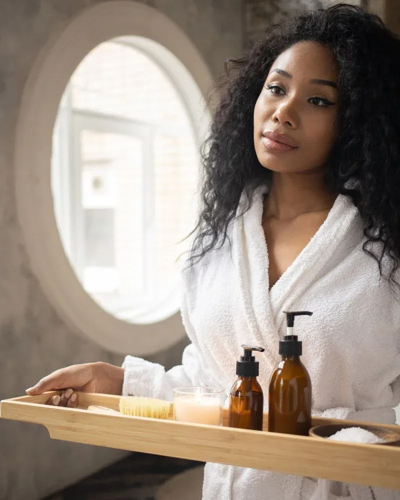 Woman in a bathrobe holding haircare products during a natural hair wash day routine.