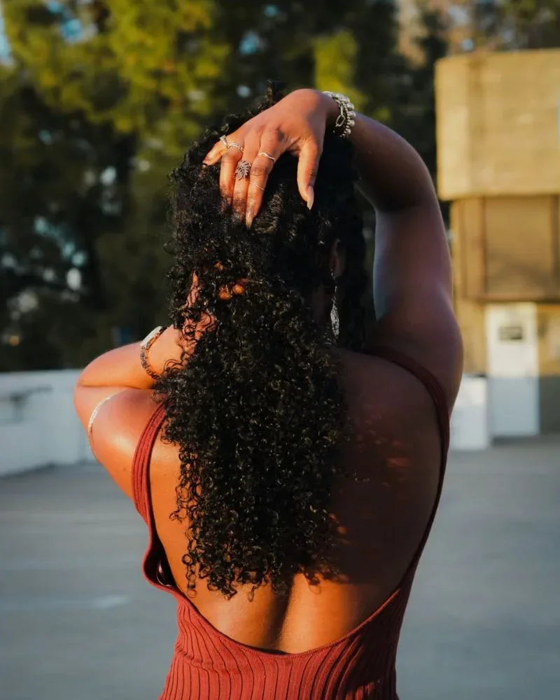 Back view of woman with defined natural curls touching her hair outdoors.