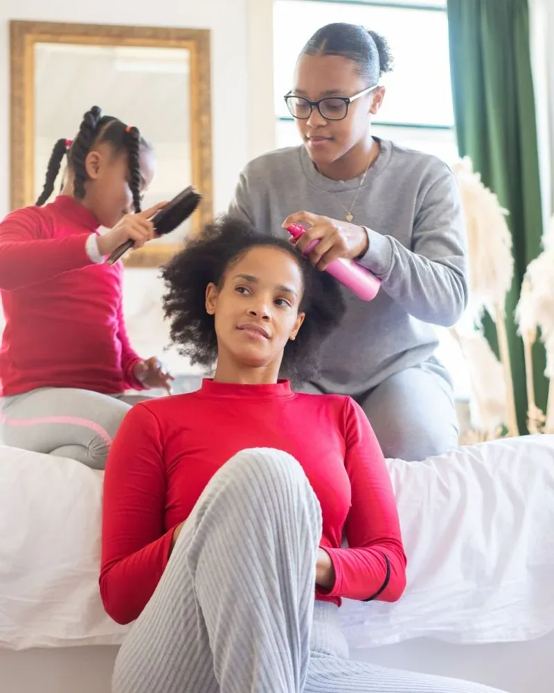 Person spraying moisture onto a woman’s natural hair