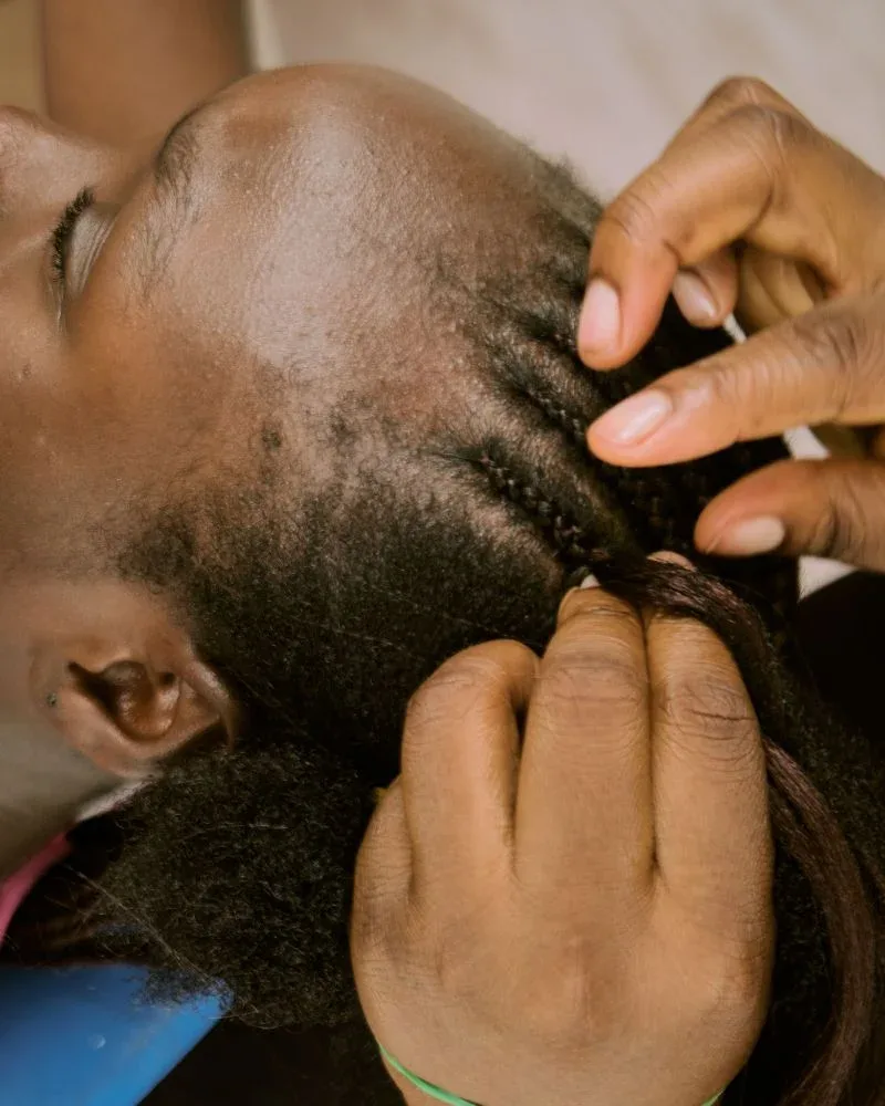 Close view of a stylist braiding natural hair near the scalp.