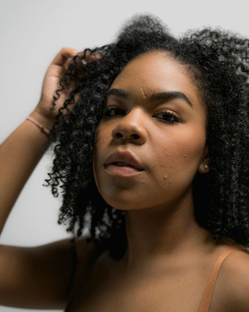 Woman with healthy Type 4 natural hair stretching a section of coily textured curls against a neutral background.