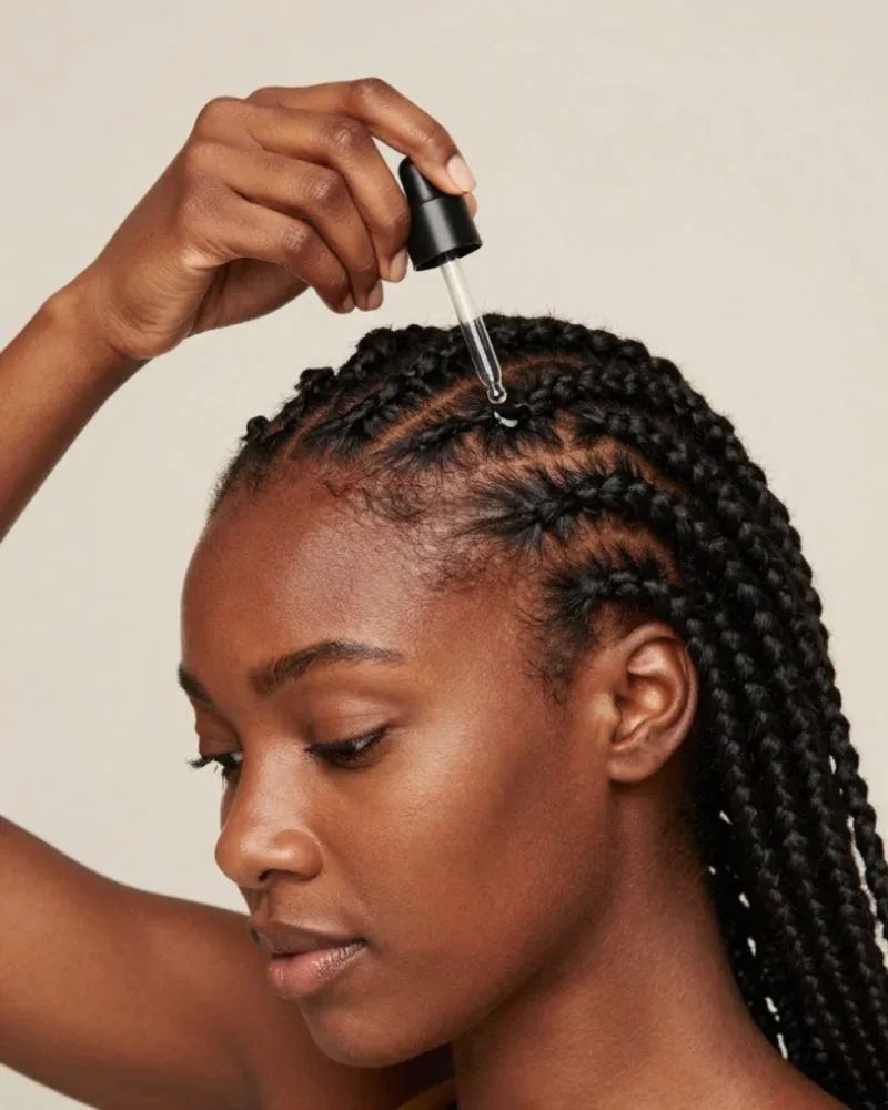 Woman with cornrows applying serum directly to her scalp using a nozzle applicator