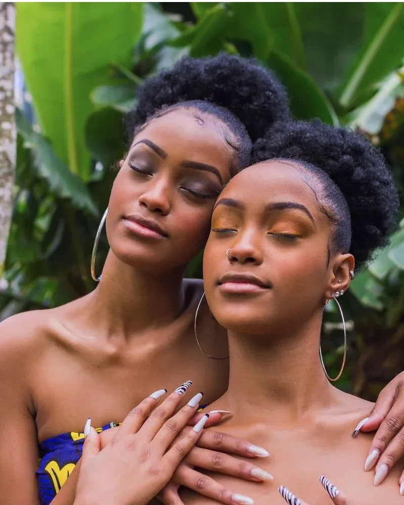 Two women with natural afro puff hairstyles representing healthy natural hair and consistent haircare