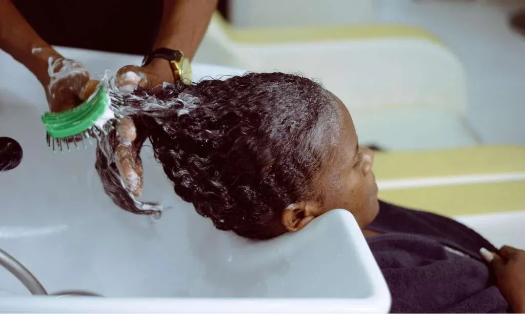 Woman washing textured hair with moisturizing shampoo at a salon wash basin