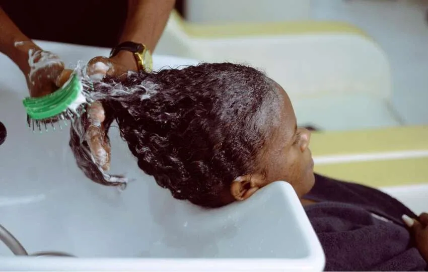 Woman washing textured hair with moisturizing shampoo at a salon wash basin