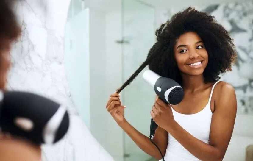 Woman using a blow dryer to stretch a section of Type 4 natural hair