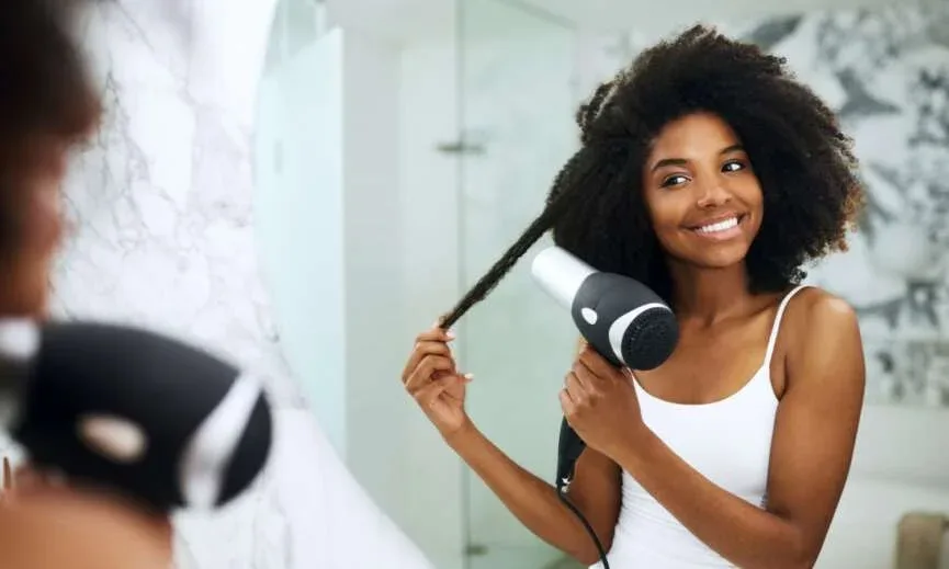 Woman using a blow dryer to stretch a section of Type 4 natural hair