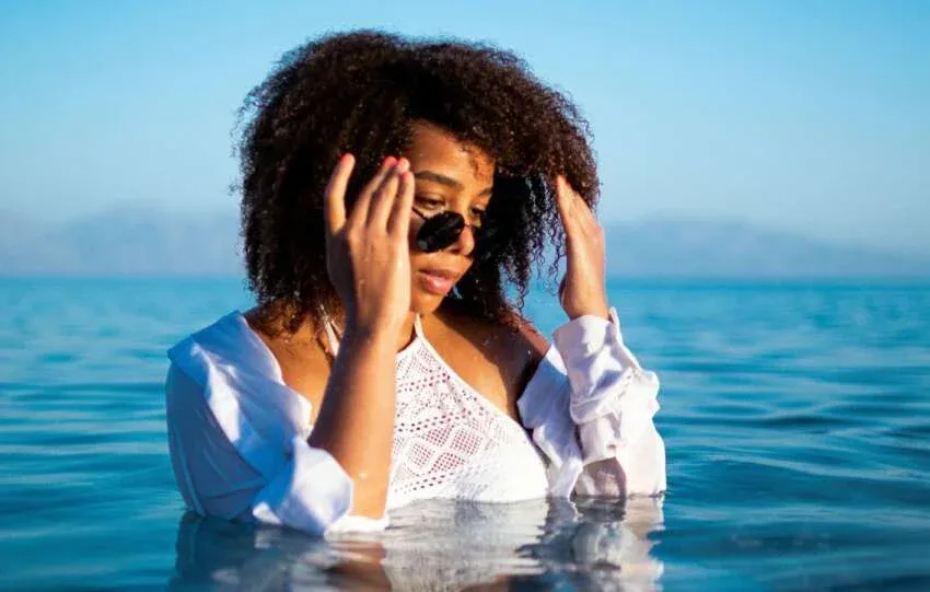 Woman touching her wet natural hair while standing in water.