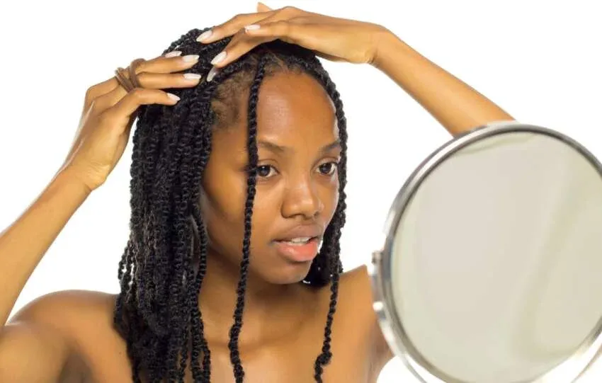 Woman with twists touching her roots while looking in a mirror.