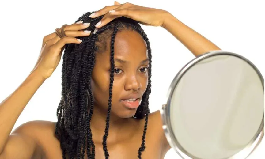Woman with twists touching her roots while looking in a mirror.