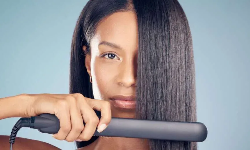 Woman using a flat iron to achieve silk press on natural hair